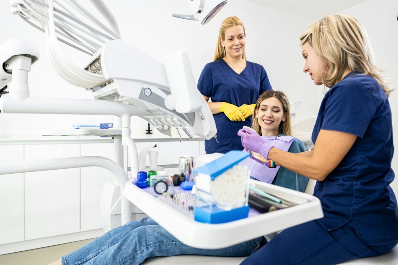 female dentist with assistant working in dental clinic examining patient teeth e1718032541269